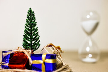 Countdown timer for Christmas, New Year and Boxing day concept. Present boxes, shopping cart, pine tree, house models and sand running through hourglass on light brown background.