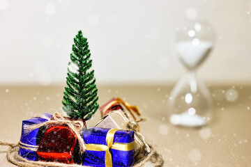 Countdown timer for Christmas, New Year and Boxing day concept. Present boxes, shopping cart, pine tree, house models and sand running through hourglass on light brown background.