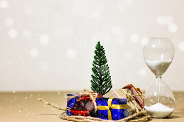 Countdown timer for Christmas, New Year and Boxing day concept. Present boxes, shopping cart, pine tree, house models and sand running through hourglass on light brown background.