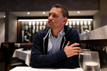 Young man sitting inside restaurant for dinner with dim lights dark atmosphere looking waiting for food waiter or date with two glasses of water