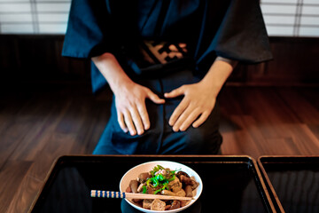 Fototapeta na wymiar Traditional Japanese house ryokan restaurant with black lacquered wood table tray and food dish closeup of mushrooms and tofu and man in kimono or yukata sitting eating