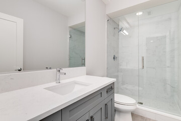 A white bathroom with a grey vanity and a white marble stand up shower.