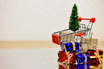 Merry Christmas, Happy New Year and Boxing day concept. Present boxes, shopping cart, pine tree and house models on light brown background.