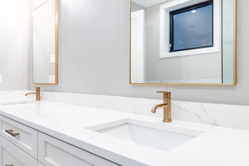 A detail shot of a white double vanity and marble counter top with gold vanity. The mirrors are lined with a gold trim. - obrazy, fototapety, plakaty