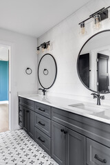 A beautiful bathroom with a dark grey vanity, circular mirrors, black light fixtures, and a pattern...