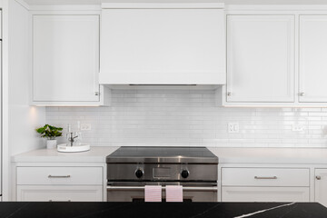 A white kitchen detail shot with a stainless steel stove and hood, subway tile backslash, black and white granite, and under cabinet lighting.