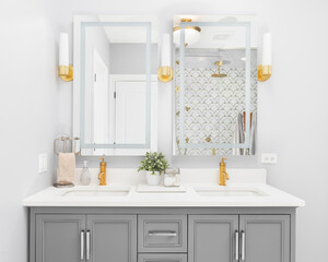 A bright, modern bathroom with a grey vanity cabinet, gold faucets and light fixtures, granite...