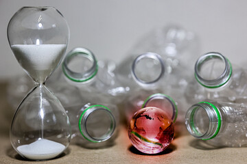 Plastic pollution. Empty plastic bottle, plastic bag and wolrd globe crystal glass with sand running through hourglass on table. Countdown timer for global warimg concept.