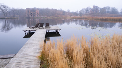 Two sunbeds on the wooden pier by the river with dry reeds next to it
