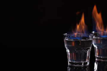 Flaming vodka in shot glasses on black background, space for text