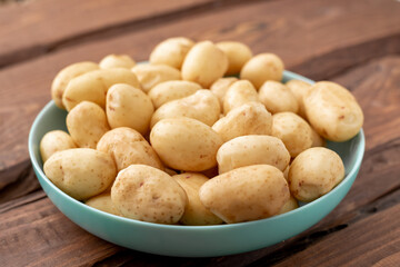 Young raw potatoes small on a plate on a brown wooden background.