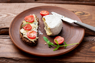Cereal bread with blue cheese and cherry tomatoes on a clay plate on a wooden background. Healthy vegetarian food.