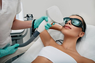 Brunette woman getting laser hair removal on her face, laser epilation to lips area. Facial laser hair removal - obrazy, fototapety, plakaty