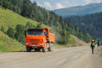 Loaded dump truck driving on a dirt mountain road with tourists on the side of the road.