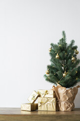 a small Christmas tree with warm bulbs in a pot on a wooden table with gifts wrapped in gold paper. the concept of Christmas