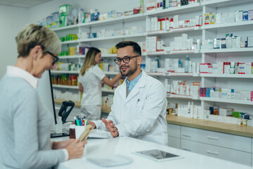 Male pharmacist selling medications at drugstore to a senior woman customer