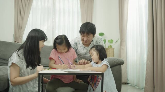 Asian Family parents play with daughters at the home table. adult parent father teaching cute small children girls learning creative activity enjoying happy high five with daddy and mom on holiday.