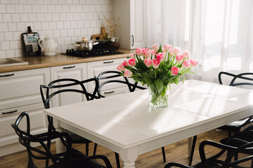 Bouquet of pink tulips in a transparent vase, on kitchen table. Flowers in interior.	