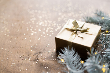 a golden gift box on a wooden table among fir branches with warm light bulbs
