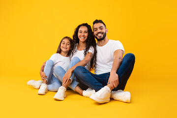 Happy Arabic Father, Mother And Daughter Embracing Sitting, Yellow Background