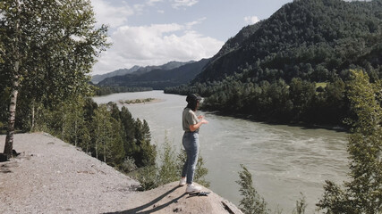 The girl raises her hands and opens a view of the river in Altai in summer.