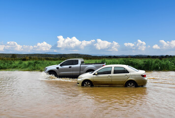 Fototapeta na wymiar Cars are passing the road which full of floodwater in rainy season, concept for car insurance and emergency events.