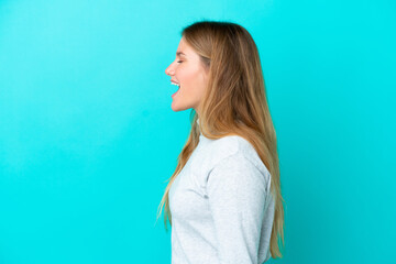 Young blonde woman isolated on blue background laughing in lateral position