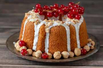 Bundt cake with icing and chopped hazelnuts decorated with red currants.