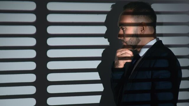 Pensive business male in suit thinking brainstorming analyzing job at gray room with jalousie shadow
