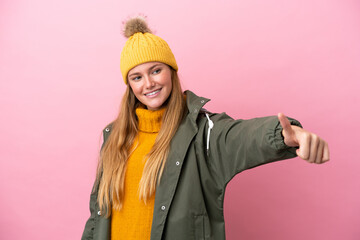 Young blonde woman wearing winter jacket isolated on pink background giving a thumbs up gesture