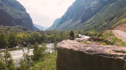 Fototapeta na wymiar A man sits on the edge of a cliff wearing a black anorak. Katu-Yaryk canyon Chulyshman Valley. Altai