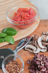 top view, close distance of a bowl of crushed tomatoes, basil leaves, sliced mushrooms and a pizza cutter, ingrediences to make a pizza, on a wood cutting board