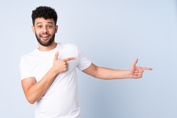 Young Moroccan man isolated on blue background surprised and pointing side - obrazy, fototapety, plakaty