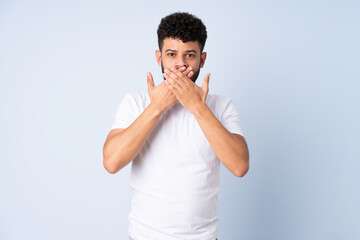 Young Moroccan man isolated on blue background covering mouth with hands