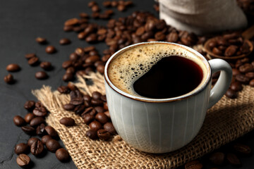 Cup of aromatic coffee and beans on black table, closeup