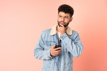 Young Moroccan man using mobile phone isolated on pink background and looking up