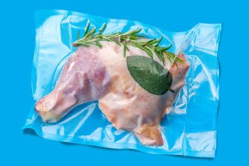 Whole chicken thighs with rosemary and sage in vacuum packed sealed for sous vide cooking isolated on blue background