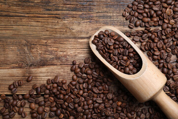 Scoop with roasted coffee beans on wooden table, flat lay. Space for text
