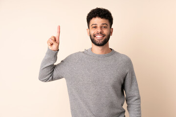 Young Moroccan man isolated on beige background pointing up a great idea