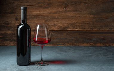 A bottle of wine and a glass of wine on a dark background.