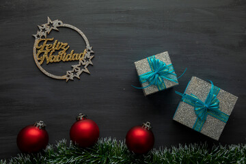 golden merry christmas sign on a black background with red spheres and gifts with blue bow.
