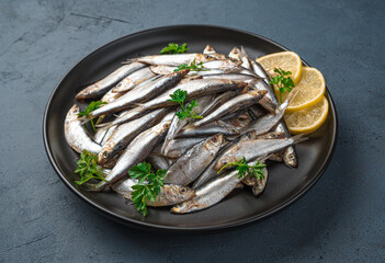 A plate of sardines with lemon and parsley on a dark background.