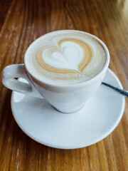 Coffee cup with heart shaped latte foam art on a wooden table at a coffee shop.
