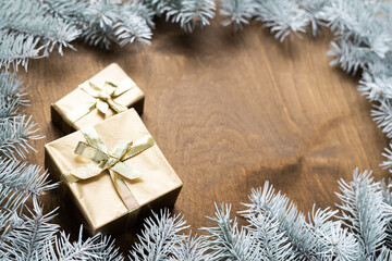 Fototapeta na wymiar a golden gift box on a wooden table among fir branches with warm light bulbs