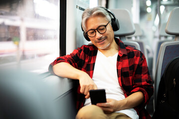 Senior man traveling by train. Man listening the music while enjoying in travel...