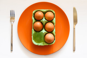Egg carton on orange plate placed on table with cutlery