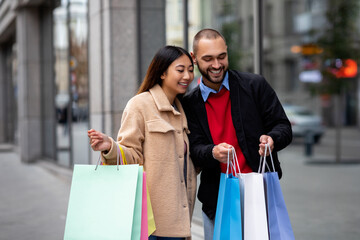 Affectionate multinational couple standing near supermarket, looking inside shopper bags, going shopping together