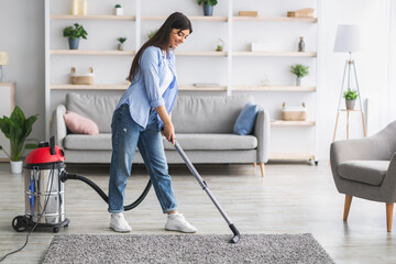 Cheerful woman cleaning rug carpet with vacuum cleaner