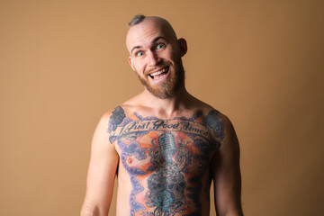 Tattooed brutal man with beard, topless naked on beige background, muscular with abs