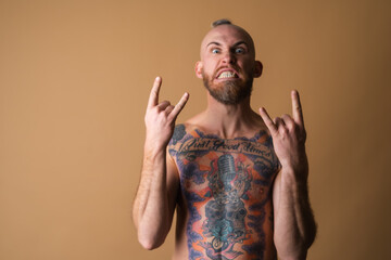 Tattooed brutal man with beard, topless naked on beige background, muscular with abs
